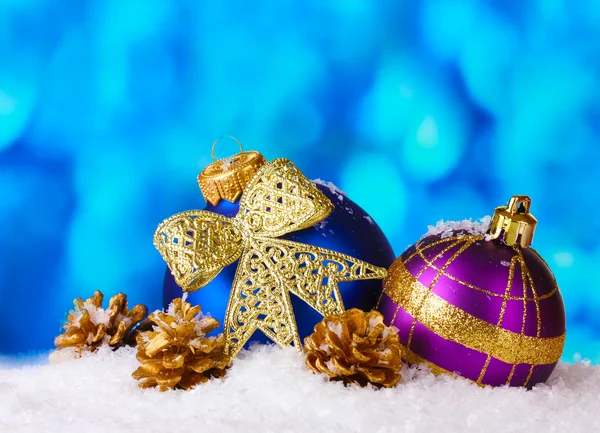 Hermosas bolas de Navidad azul y púrpura y conos en la nieve en el backgro azul — Foto de Stock