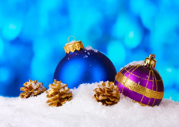 Vackra blå och lila julgranskulor och kottar i snö på blå backgro — Stockfoto