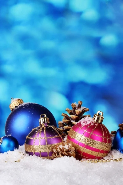 Schöne helle Weihnachtskugeln und Zapfen auf Schnee auf blauem Hintergrund — Stockfoto