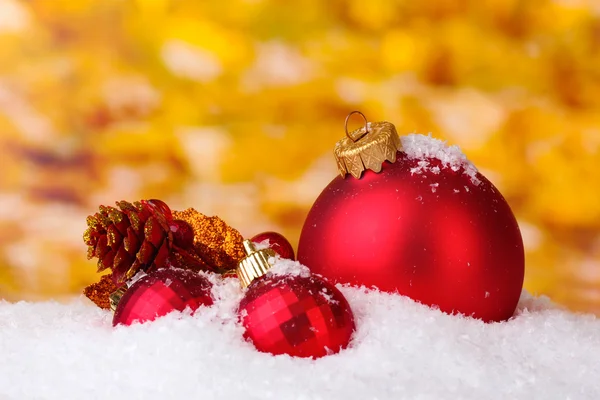 Beautiful red Christmas balls and branch in snow on yellow background — Stock Photo, Image