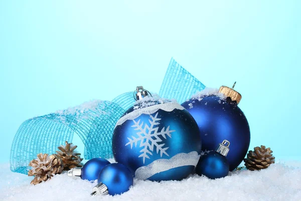 Schöne blaue Weihnachtskugeln und Zapfen im Schnee auf blauem Hintergrund — Stockfoto