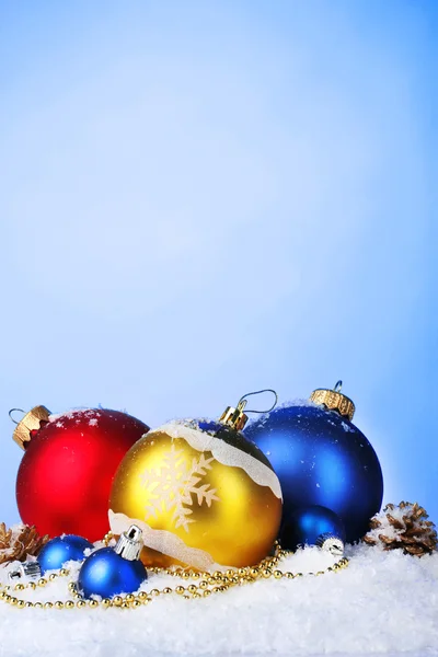 Hermosas bolas de Navidad brillantes y conos en la nieve sobre fondo azul —  Fotos de Stock