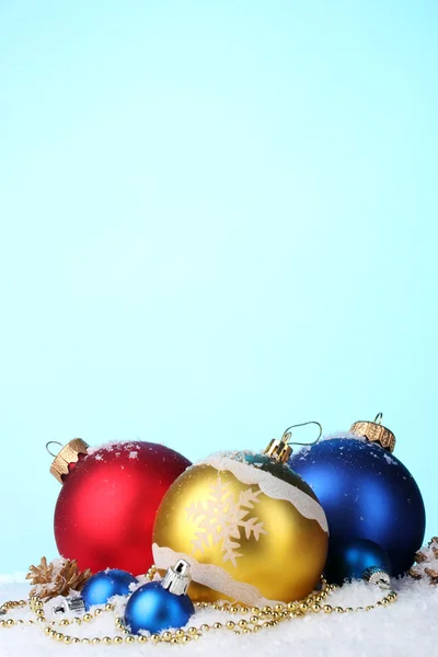 Beautiful bright Christmas balls and cones in snow on blue background — Stock Photo, Image