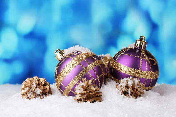 Hermosas bolas de Navidad púrpura y conos en la nieve sobre fondo azul —  Fotos de Stock
