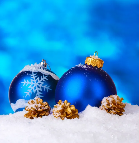 Красиві блакитні різдвяні кульки і шишки в снігу на синьому фоні — стокове фото