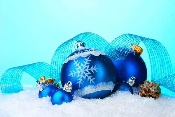 Prachtige blauwe kerstballen en kegels in sneeuw op blauwe achtergrond — Stockfoto