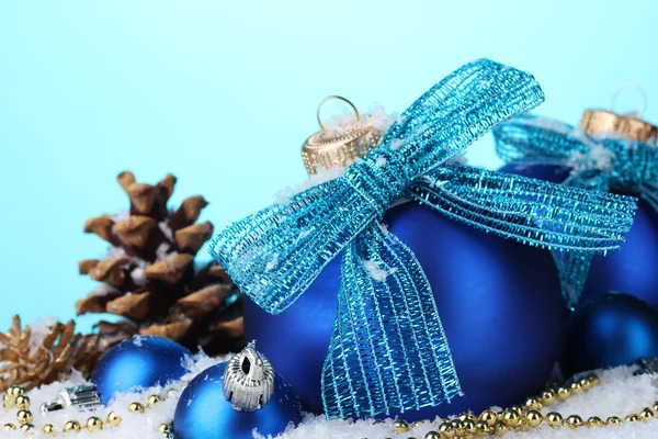Schöne blaue Weihnachtskugeln und Zapfen auf Schnee auf blauem Hintergrund — Stockfoto