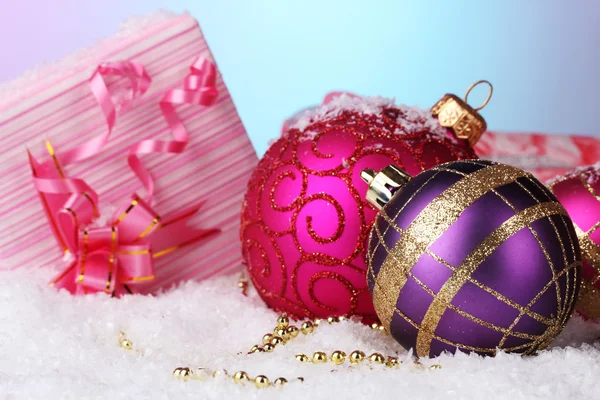 Beautiful Christmas balls and gifts on snow on bright background — Stok fotoğraf