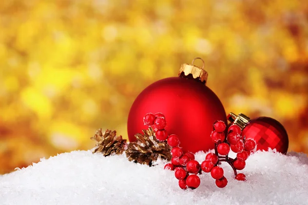 Vackra röda julgranskulor och kottar på snö på gul bakgrund — Stockfoto