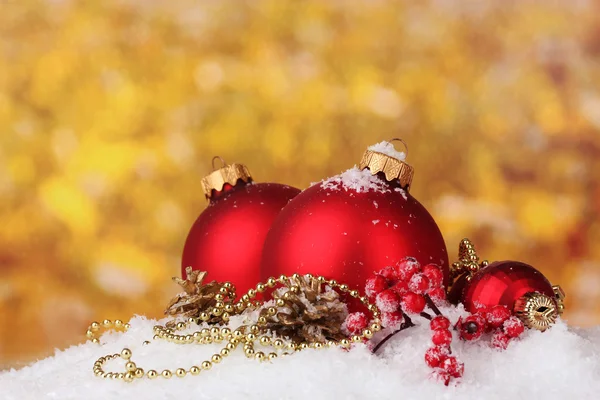 Beautiful red Christmas balls and cones on snow on yellow background — Stock Photo, Image