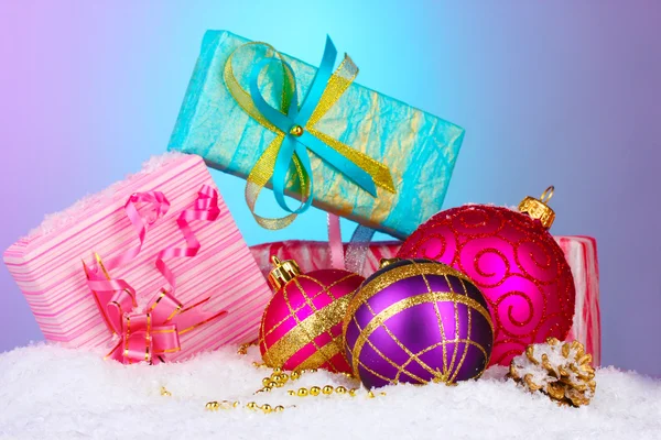 Beautiful Christmas balls and gifts on snow on bright background — Stockfoto