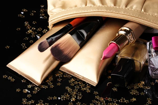 Hermosa bolsa de maquillaje dorado y cosméticos aislados en negro — Foto de Stock