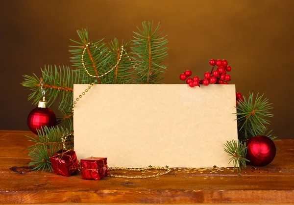Prázdná pohlednice, vánoční koule a jedle na dřevěný stůl na hnědé pozadí — Stock fotografie