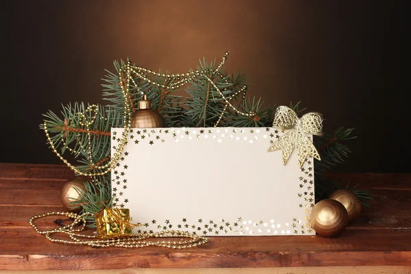Prázdná pohlednice, vánoční koule a jedle na dřevěný stůl na hnědé pozadí — Stock fotografie