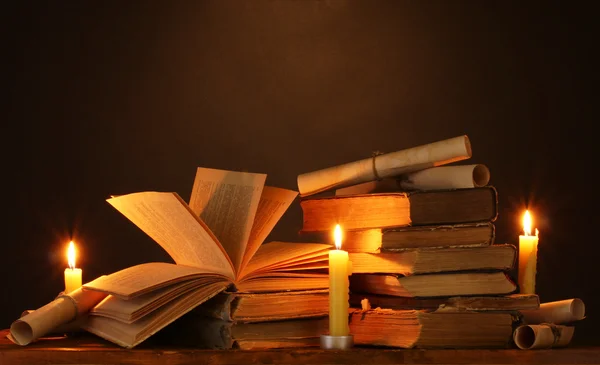 Stapel alter Bücher mit Kerze und Schriftrolle im Dunkeln — Stockfoto