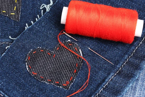 Heart-shaped patch on jeans wiht needle and thread closeup — Stock Photo, Image