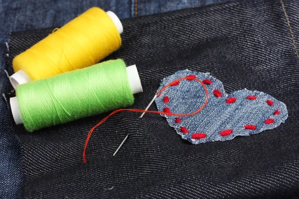 Пластырь в форме сердца на джинсах с нитками и иглой крупным планом — стоковое фото