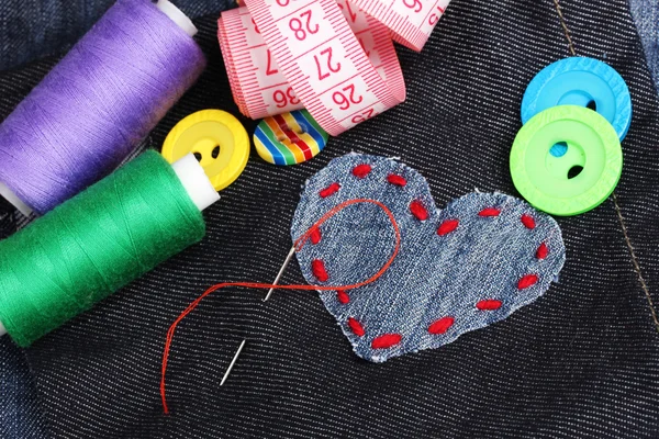 Heart-shaped patch on jeans with threads and buttons closeup — Stock Photo, Image