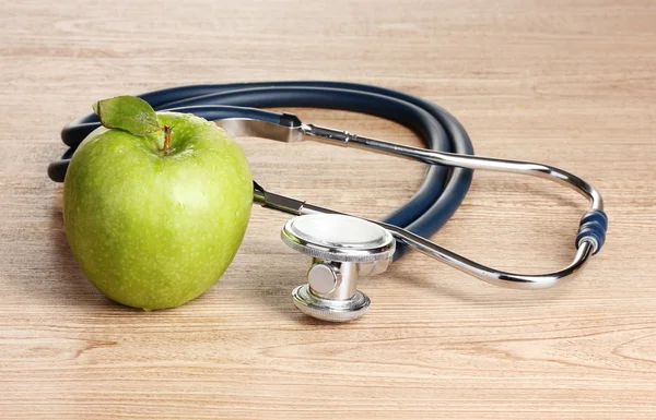 Medische stethoscoop en groene appel op houten achtergrond — Stockfoto