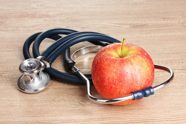 Stéthoscope médical et pomme rouge sur fond en bois — Photo