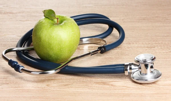 Medical stethoscope and green apple on wooden background — Stock Photo, Image