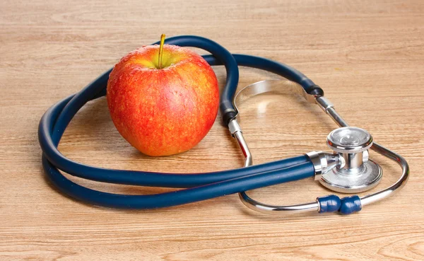 Sağlık stetoskop ve ahşap zemin üzerinde kırmızı elma — Stok fotoğraf