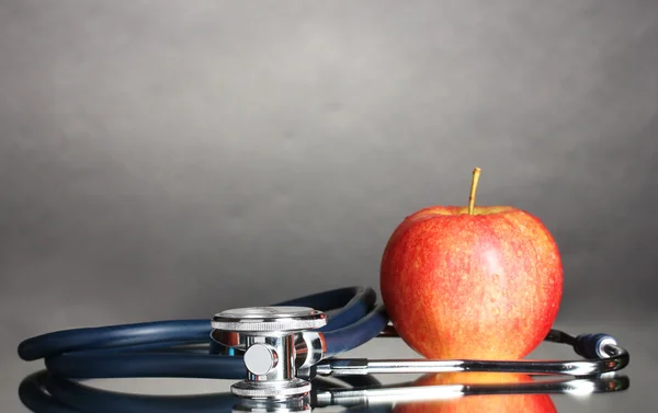 Медичний стетоскоп і червоне яблуко на сірому — стокове фото