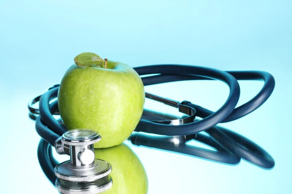Estetoscópio médico e maçã verde em azul — Fotografia de Stock