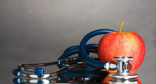 Medical stethoscope and red apple on grey — Stock Photo, Image