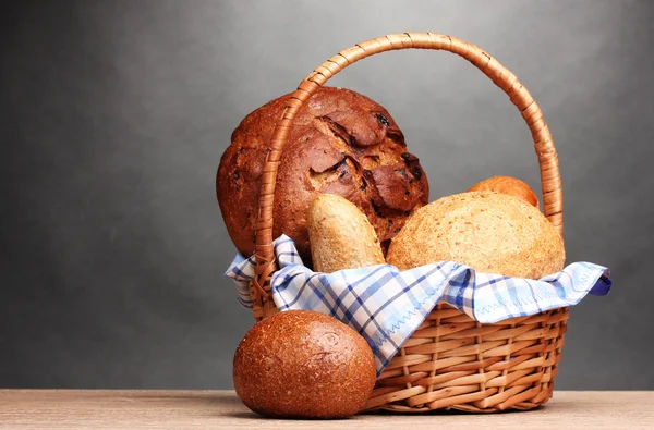 Delicioso pan en cesta sobre mesa de madera sobre fondo gris — Foto de Stock