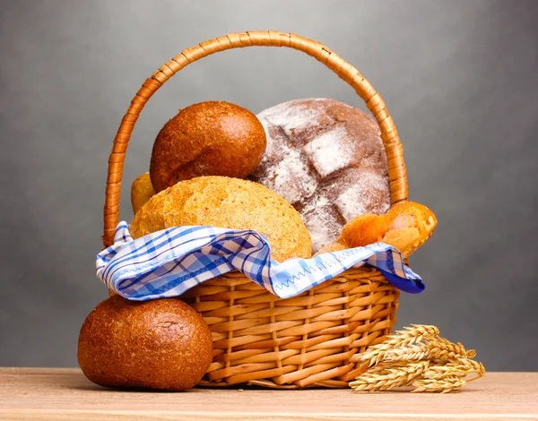 Heerlijk brood in mand en oren op houten tafel op grijze achtergrond — Stockfoto