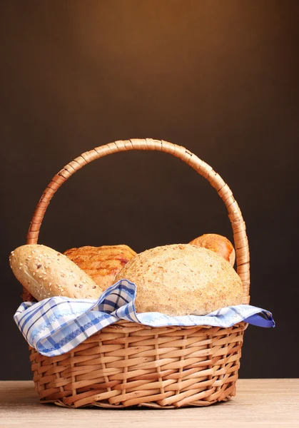 Heerlijk brood in mand op houten tafel op bruine achtergrond — Stockfoto