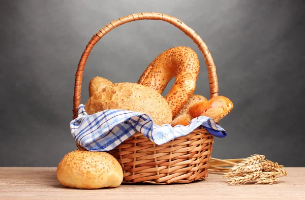 Pâine delicioasă în coș și urechi pe masă de lemn pe fundal gri — Fotografie, imagine de stoc