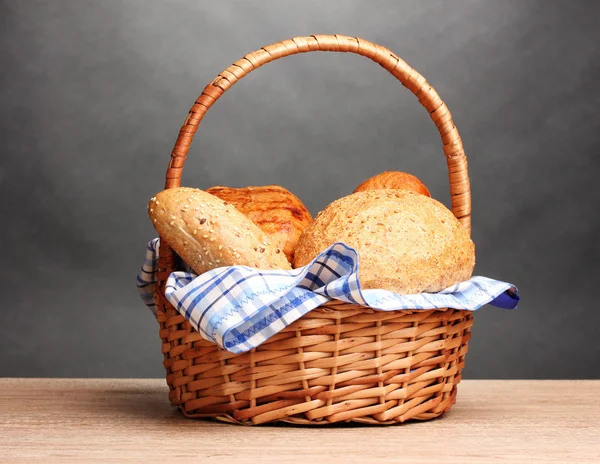Heerlijk brood in mand op houten tafel op grijze achtergrond — Stockfoto