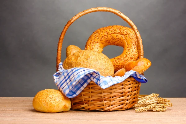 Delicioso pan en cesta y orejas sobre mesa de madera sobre fondo gris — Foto de Stock