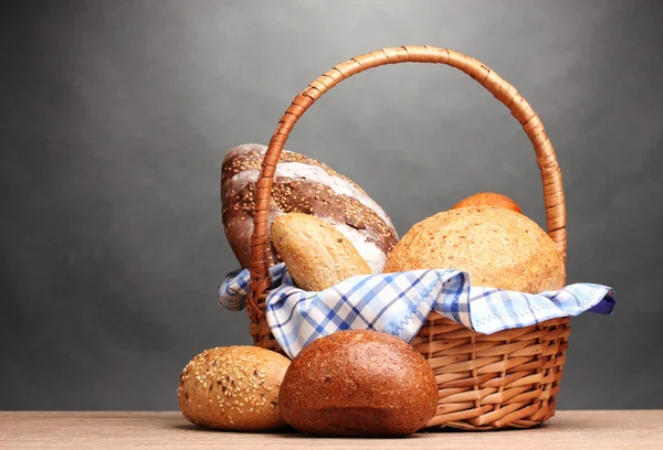 Delicioso pan en cesta sobre mesa de madera sobre fondo gris —  Fotos de Stock