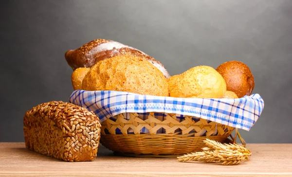 Νόστιμο ψωμί στο καλάθι και αυτιά στο ξύλινο τραπέζι σε γκρι φόντο — Φωτογραφία Αρχείου