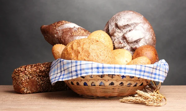 Νόστιμο ψωμί στο καλάθι και αυτιά στο ξύλινο τραπέζι σε γκρι φόντο — Φωτογραφία Αρχείου
