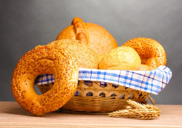 Смачний хліб у кошику та вухах на дерев'яному столі на сірому фоні — стокове фото
