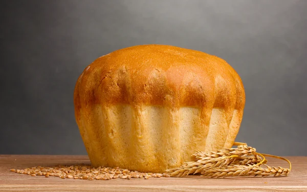 Вкусный круглый хлеб и уши на деревянном столе на сером фоне — стоковое фото