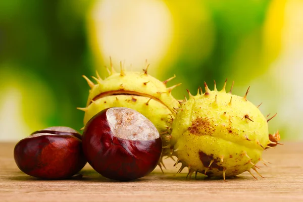 Green and brown chestnuts on wooden table on green background — Stock Photo, Image