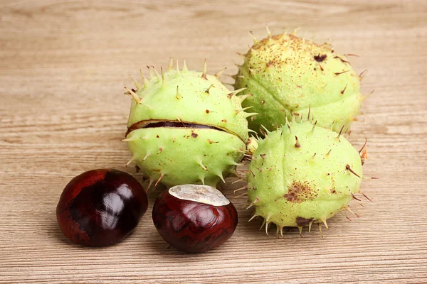 Green and brown chestnuts on wooden background — Stock Photo, Image