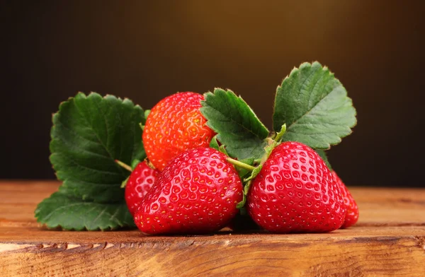 Strawberries with leaves on wooden table on brown background — Stock Photo, Image