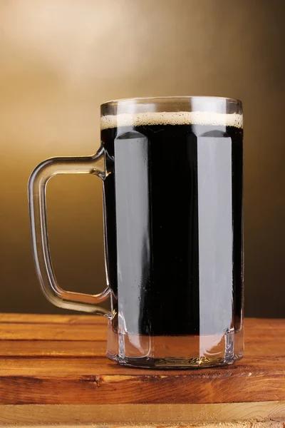 Mörkt öl i en mugg på träbord på brun bakgrund — Stockfoto