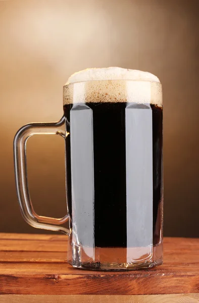 Koyu kahverengi zemin üzerine ahşap masa üzerinde bir kupa bira — Stok fotoğraf
