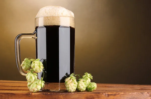 黑啤在棕色背景上的木桌上跃杯和绿色的点 — 图库照片