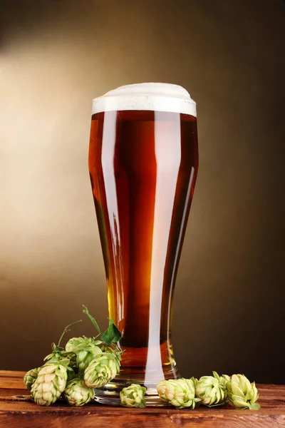 Cerveza en vidrio y lúpulo verde sobre mesa de madera sobre fondo marrón — Foto de Stock