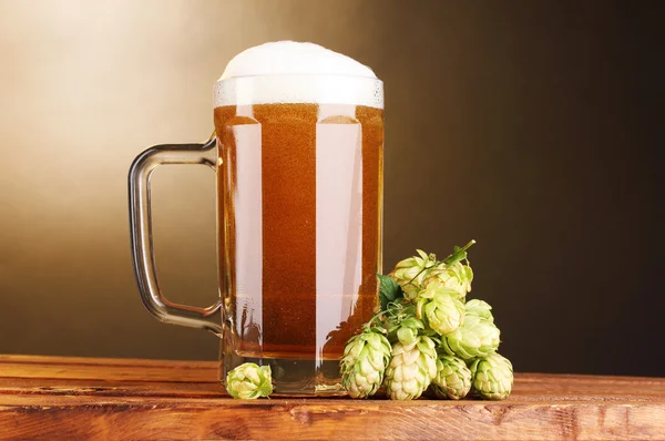 Кружка пива и зеленый прыжок на деревянный стол на коричневом фоне — стоковое фото