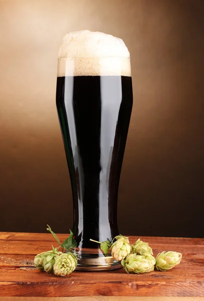 黑啤在棕色背景上的木桌上的玻璃和绿色跃点 — 图库照片