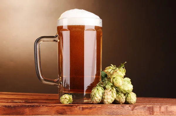 Jarra de cerveza y lúpulo verde sobre mesa de madera sobre fondo marrón — Foto de Stock